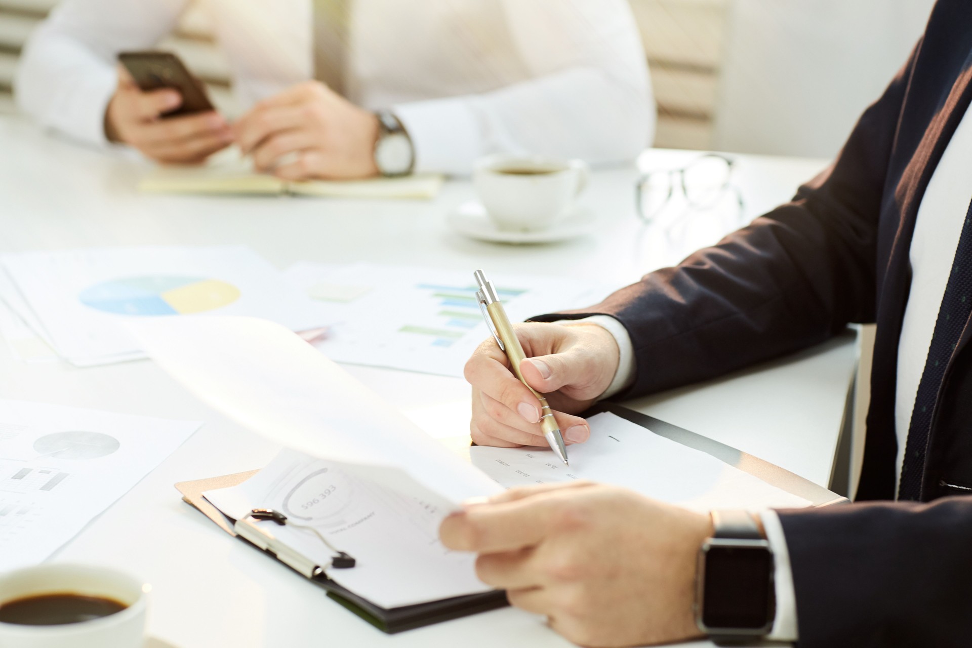 Primo piano dell'imprenditore irriconoscibile in abito formale seduto al tavolo della conferenza e analizzando i dati finanziari alla riunione